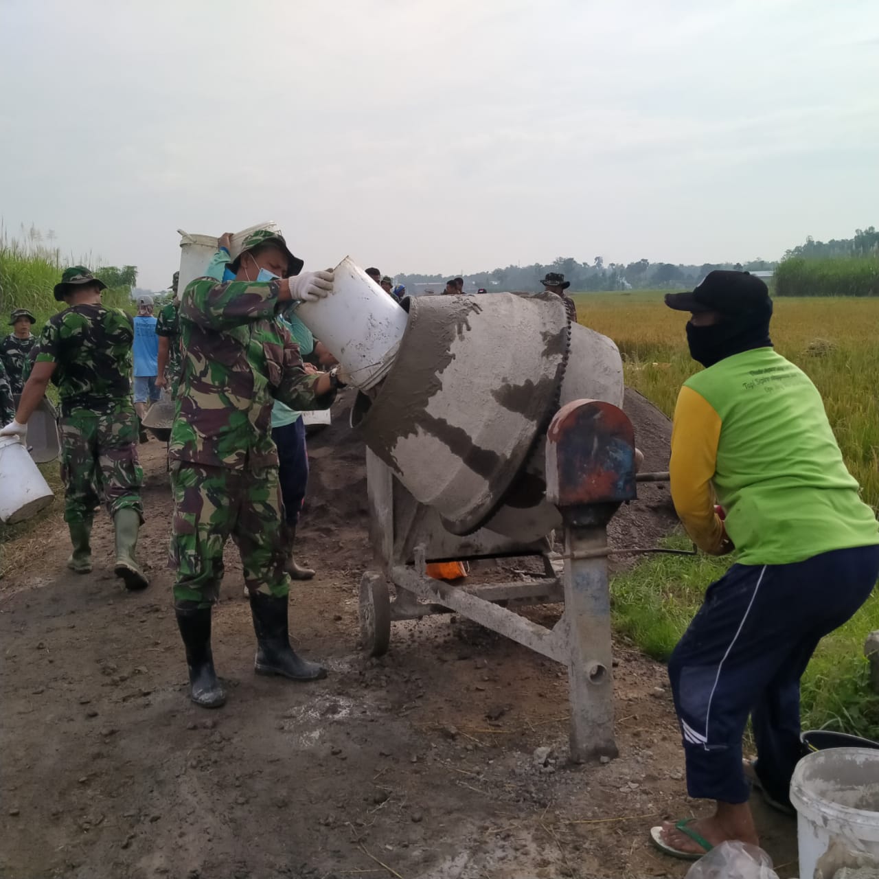 Silih Berganti  Anggota Satgas TMMD Tuangkan Material Ke Dalam Tungku Mesin  Molen